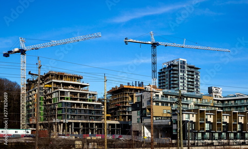 New construction of high-rise buildings in Burnaby city, industrial construction site, construction equipment, several construction cranes on the background of finished skyscrapers and blue sky wit
