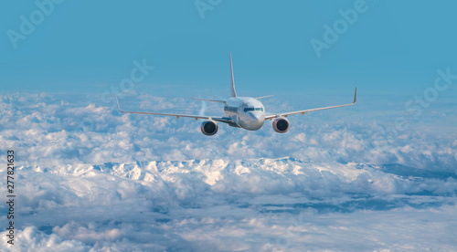 An airplane is flying over low clouds and city with blue sea - White commercial airplane flying over city