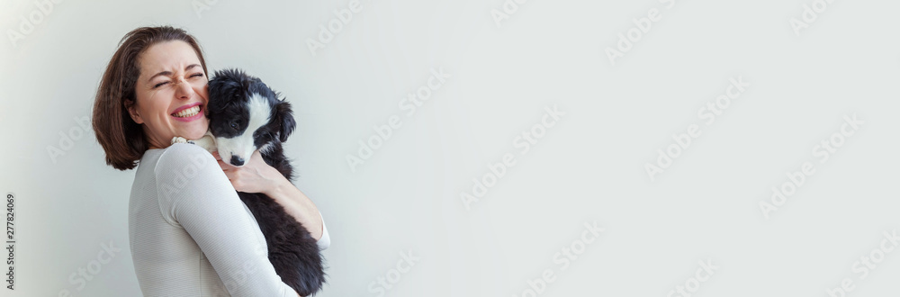 Smiling young attractive woman embracing cute puppy dog border collie isolated on white background. Girl huging new lovely member of family. Pet care and animals concept. Banner - obrazy, fototapety, plakaty 