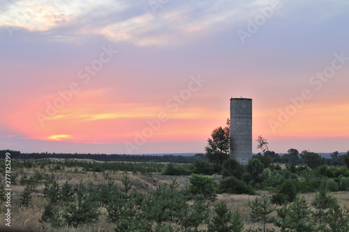 Brick tower on the background of a beautiful sunset. Evening Donbass steppe landscape. Young pines in the foreground
