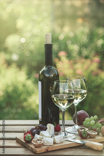 Fototapeta Naklejka Na Ścianę i Meble -  Two glasses of white wine,  cheese, fruits. Romantic outdoor dinner in a garden