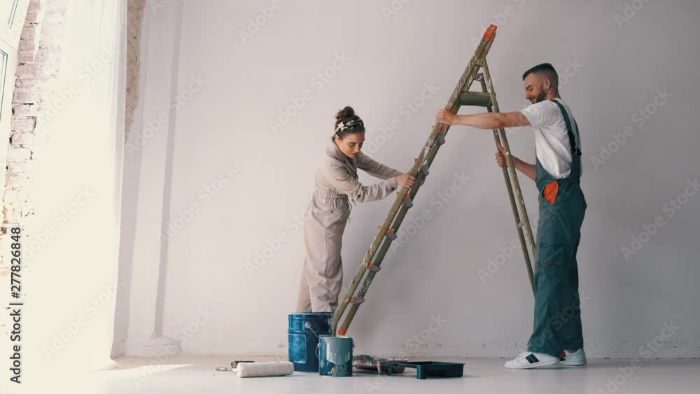 wife standing on a ladder while her husband paints the wall and helps her wife standing on a ladder while her husband paints the wall and helps her