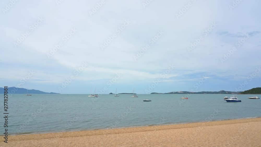 Static slow motion shot of the sea waves hitting the sandy tropical beach with boats scattered around the sea Static slow motion shot of the sea waves hitting the sandy tropical beach with boats scattered around the sea