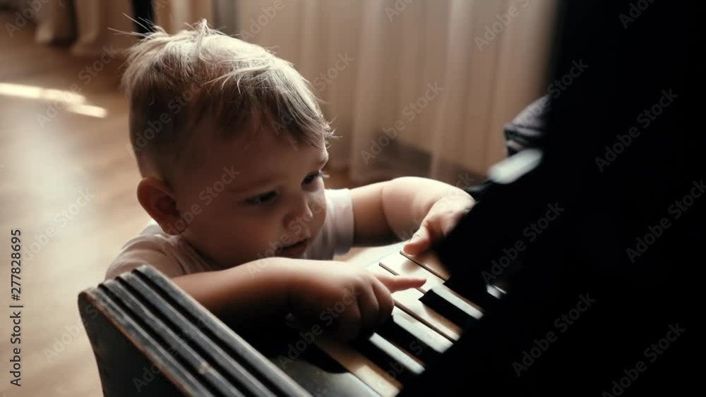 Little cute baby boy with smile on his face knocking on piano keys in slow motion. Child trying to play piano at home. Curious little guy. Little cute baby boy with smile on his face knocking on piano keys in slow motion. Child trying to play piano at home. Curious little guy.