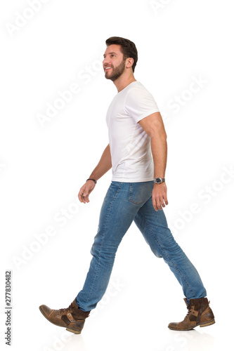 Smiling Man In White T-shirt, Jeans And Boots Is Walking And Looking Up