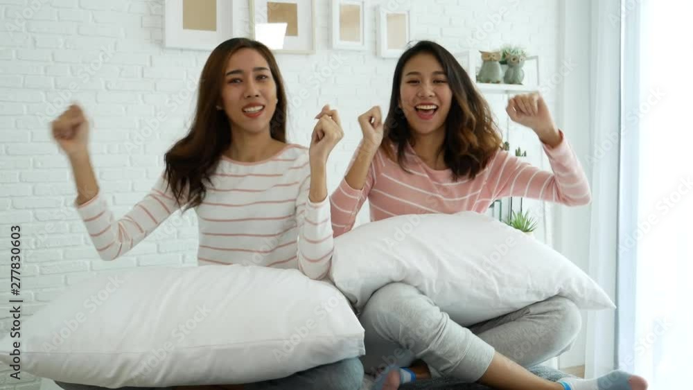 Two young women dance laughing together happy friendship smile with happiness in bedroom wear casual dress on bed. Happy girl friends dance to celebrate good news together at home Two young women dance laughing together happy friendship smile with happiness in bedroom wear casual dress on bed. Happy girl friends dance to celebrate good news together at home