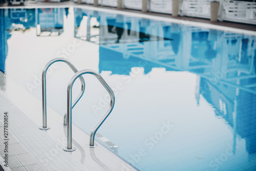 Stylish blue pool with metal ladder close up at modern hotel. Summer vacation and relax concept. Beautiful water surface, space for text