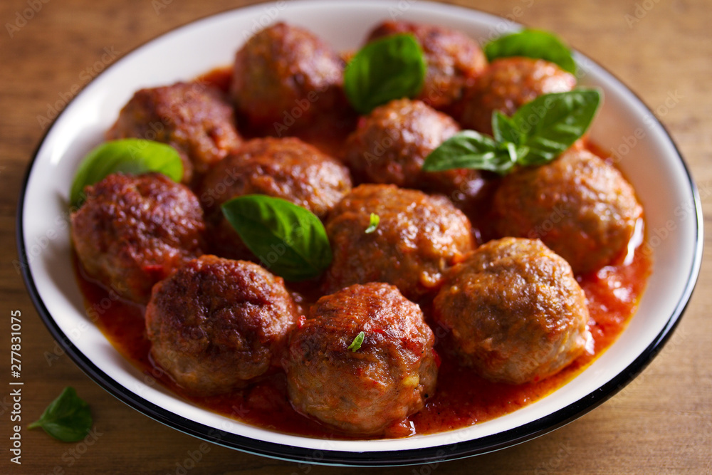 Meatballs in tomato sauce, garnished with basil in bowl on wooden table Meatballs in tomato sauce, garnished with basil in bowl on wooden table