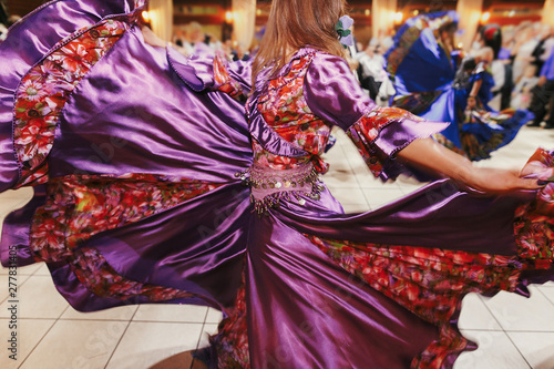Beautiful gypsy girls dancing in traditional purple floral dress at wedding reception in restaurant. Woman performing romany dance and folk songs in national clothing. Roma gypsy festival