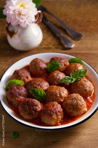Meatballs in tomato sauce, garnished with basil in bowl on wooden table