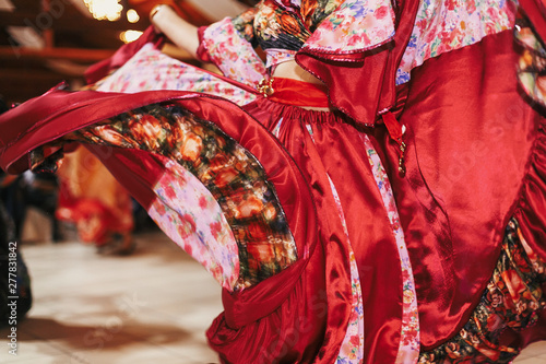 Beautiful gypsy girls dancing in traditional red floral dress at wedding reception in restaurant. Woman performing romany dance and folk songs in national clothing. Roma gypsy festival