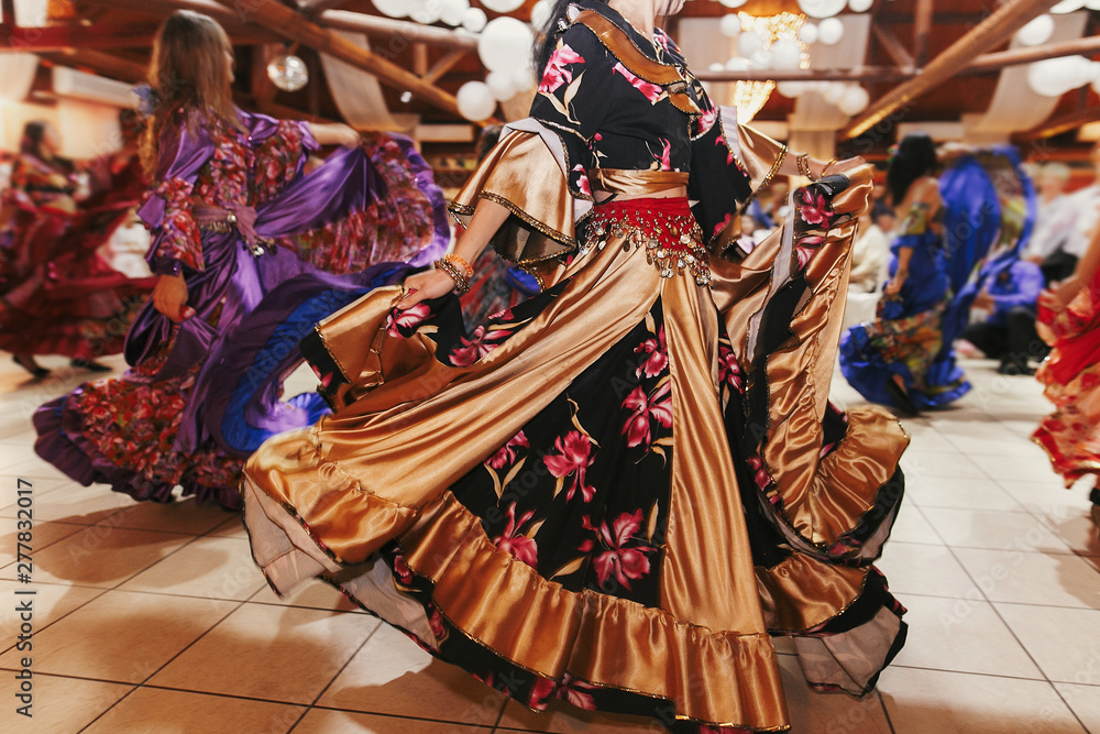 Beautiful gypsy girls dancing in traditional gold floral dress at wedding reception in restaurant. Woman performing romany dance and folk songs in national clothing. Roma gypsy festival