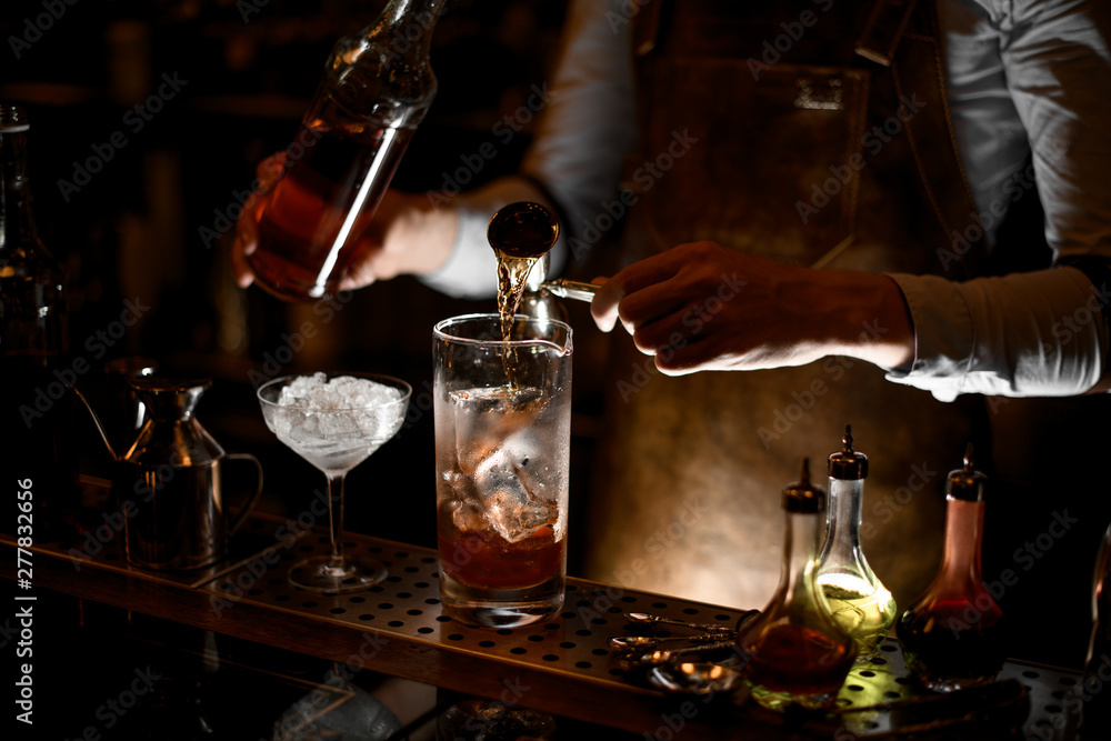 Bartender pouring an alcohol from the steel jigger to the measuring glass cup