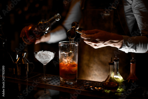 Professional male bartender pouring an alcohol from the steel jigger to the measuring glass cup
