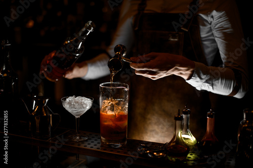 Bartender pouring an alcoholic drink from the steel jigger to the measuring glass cup