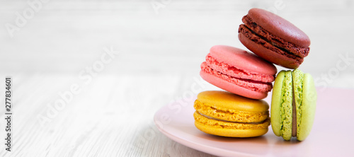 Tablou canvas Sweet and colorful macarons on a pink plate over white wooden background, side view