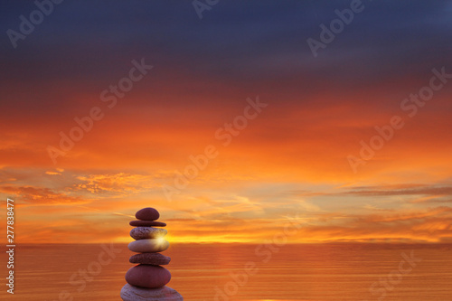 colored stones pebbles lined up with a pyramid on the background of the sea at sunset  Zen  harmony  balance. ocean at sunset in the background
