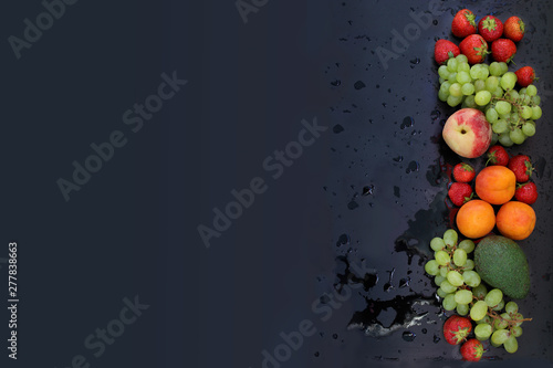 fresh juicy strawberries, grapes, peaches, apricots, avocados on a black wet background in splashes and drops of water, top view