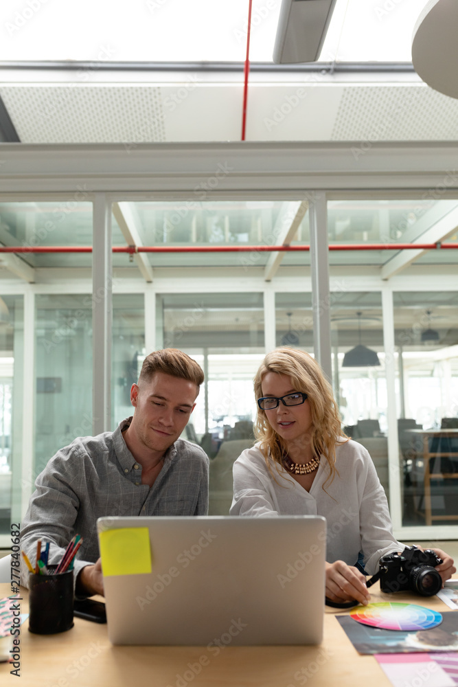 Male and female graphic designers discussing over laptop at desk Male and female graphic designers discussing over laptop at desk