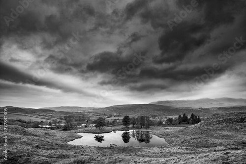 Stunning landscape image of dramatic storm clouds over Kelly Hall Tarn in Lake District during late Autumn Fall afternoon photo