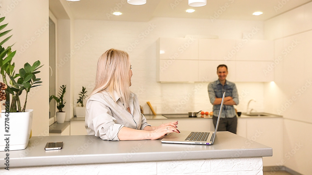 Business couple in kitchen, man preparing breakfast, woman using laptop Business couple in kitchen, man preparing breakfast, woman using laptop