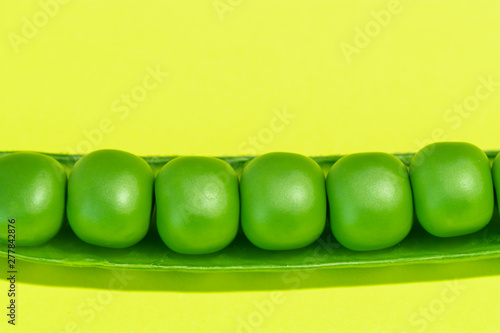 Fresh green pea pods and peas on the yellow background.