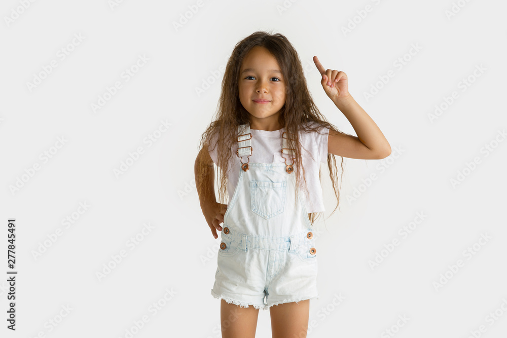 Beautiful female half-length portrait isolated on white studio background. Little emotional asian girl wearing white. Facial expression, human emotions, advertising concept. Pointing up. Beautiful female half-length portrait isolated on white studio background. Little emotional asian girl wearing white. Facial expression, human emotions, advertising concept. Pointing up.