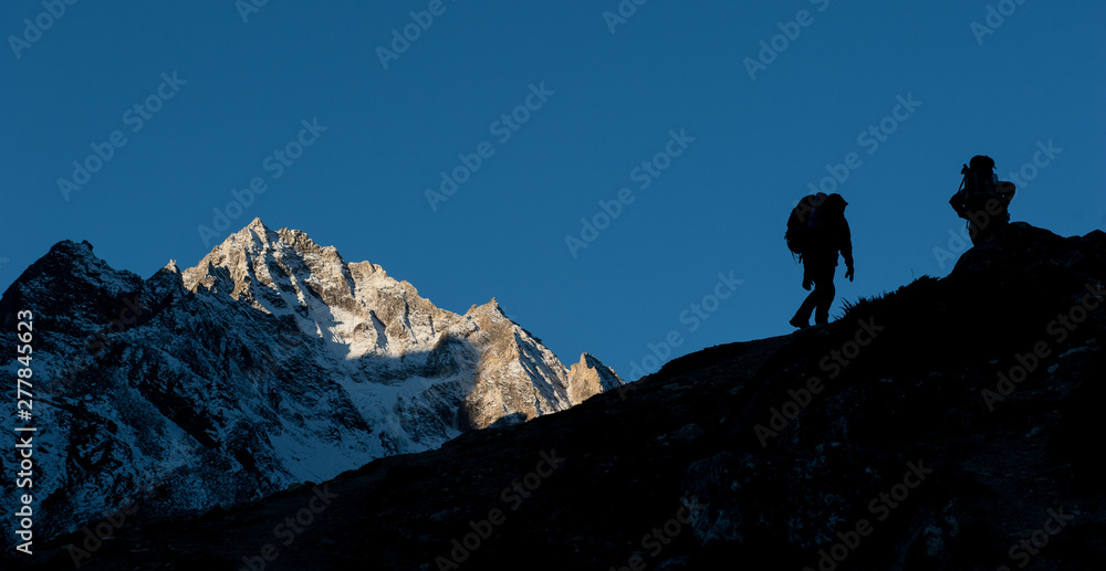 Young woman and man with backpacks walking to the pass on Manaslu circuit with view of Mount Manaslu range 8 156 meters. Trekkers in Himalayas, Manaslu Glacier in Gorkha District, Nepal. Sunny day.