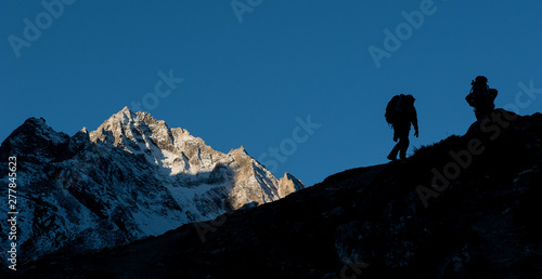 Young woman and man with backpacks walking to the pass on Manaslu circuit with view of Mount Manaslu range 8 156 meters. Trekkers in Himalayas, Manaslu Glacier in Gorkha District, Nepal. Sunny day. © baisa