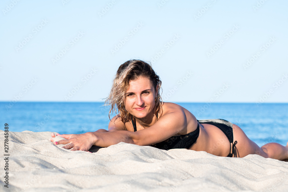 tanned young attractive woman with curly hair in black swimsuit on the beach, lying on the sand tanned young attractive woman with curly hair in black swimsuit on the beach, lying on the sand