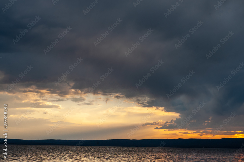 A setting sun is peaking through the clouds over lake Yellowstone on a summer's evening.