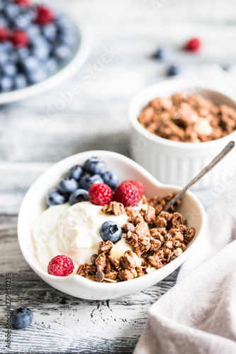 Greek yogurt, blueberries, raspberries and granola in a white bowl on a wooden background