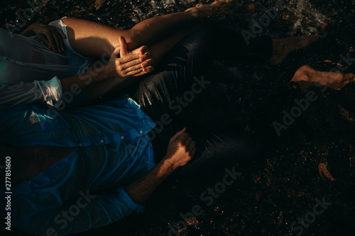 Wet couple lying on the shore and holding hands.