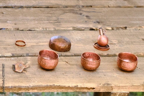 Dishes of copper on a wooden table. Bronze things from vintage patterns. Cups, rings, handmade copper jewelry, retro style. photo