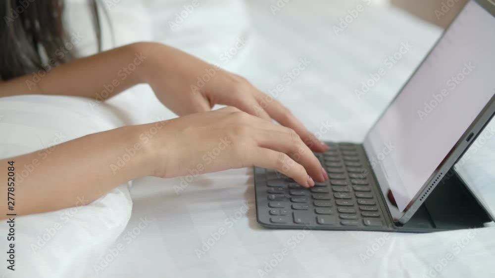 Close up hand asian woman touching keyboard on modern digital tablet on the bed in her home Close up hand asian woman touching keyboard on modern digital tablet on the bed in her home