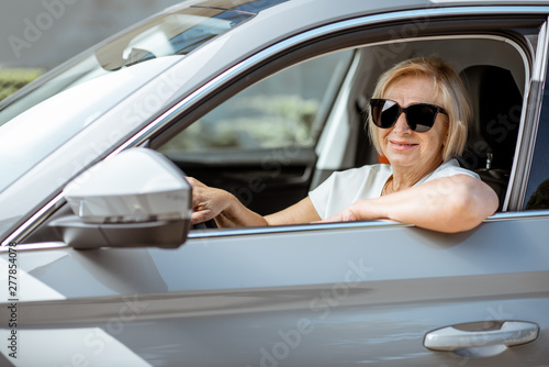Portrait of a senior woman driver sitting in the modern car, looking out the window. Concept of an active people during retirement age