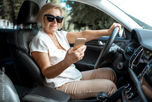 Senior business woman using smart phone while driving a car, view from the inside of a vehicle. Concept of an active people during retirement age © rh2010