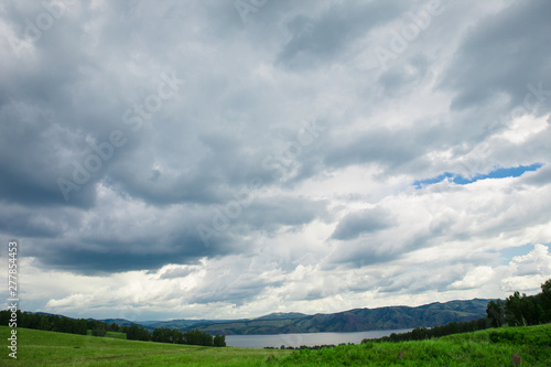 Blue sky with white clouds, fields and meadows with green grass, on the background of mountains. Composition of nature. Rural summer landscape. © Елена Труфанова