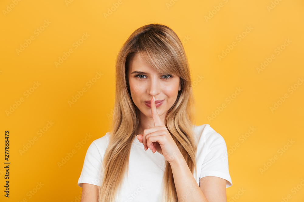 Serious young blonde woman posing isolated over yellow wall background dressed in white casual t-shirt showing silence gesture. Serious young blonde woman posing isolated over yellow wall background dressed in white casual t-shirt showing silence gesture.