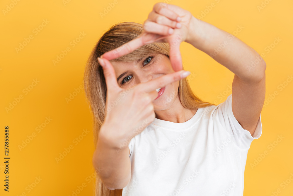 Happy young pretty blonde woman posing isolated over yellow wall background dressed in white casual t-shirt showing photo frame gesture.