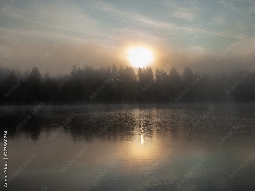 Foggy and mystical lake landscape before sunrise. All silhouettes are blurry and unclear. Vaidavas lake, Latvia