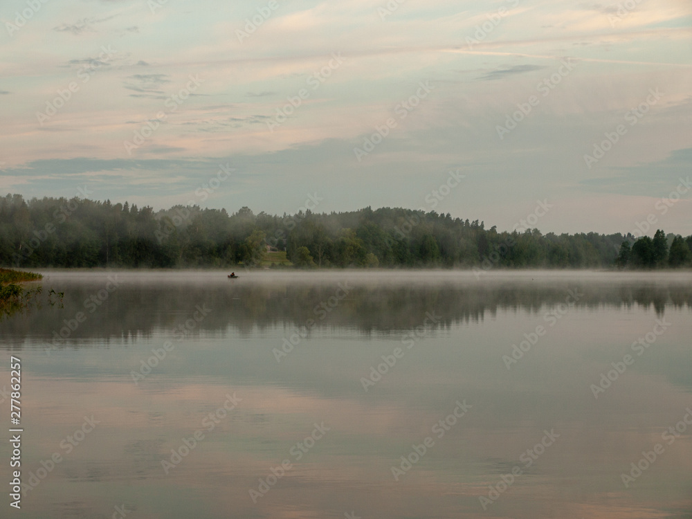 Fototapeta premium Foggy and mystical lake landscape before sunrise. All silhouettes are blurry and unclear. Vaidavas lake, Latvia
