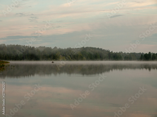 Foggy and mystical lake landscape before sunrise. All silhouettes are blurry and unclear. Vaidavas lake, Latvia