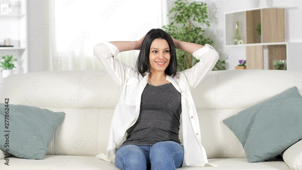 Front view of a happy woman relaxing sitting on a couch at home Front view of a happy woman relaxing sitting on a couch at home