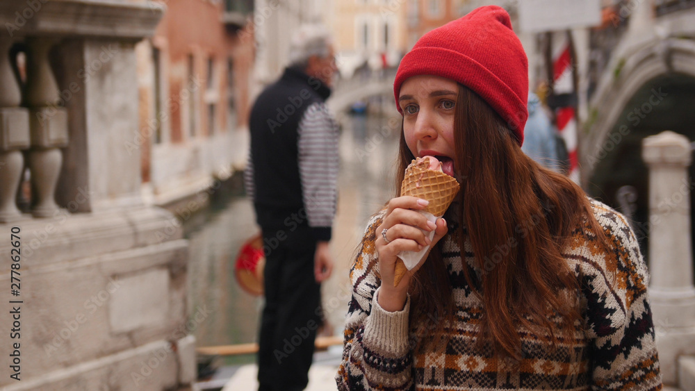 Young woman lick the icecream while walking on the Venice streets