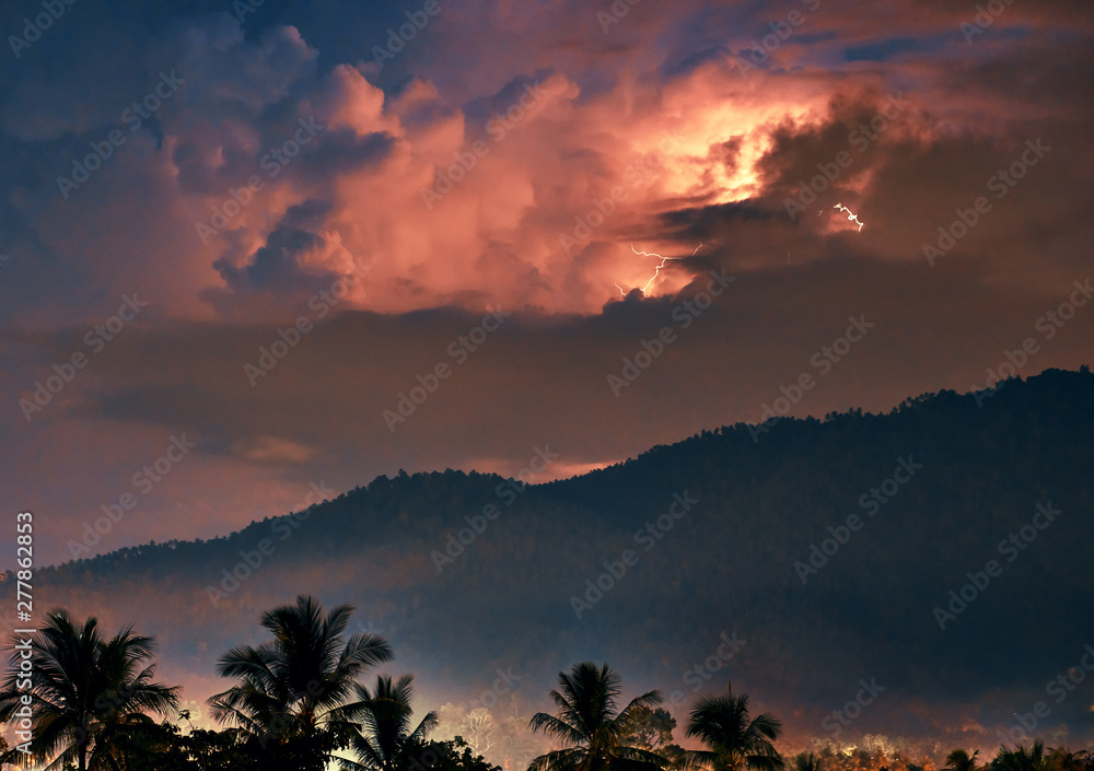 Thunderstorm and lightning over mountain and palm trees on a tropical island