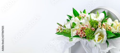 A box with white tulips and ornamental plants on a white background. Spring flowers.  Place for text. 