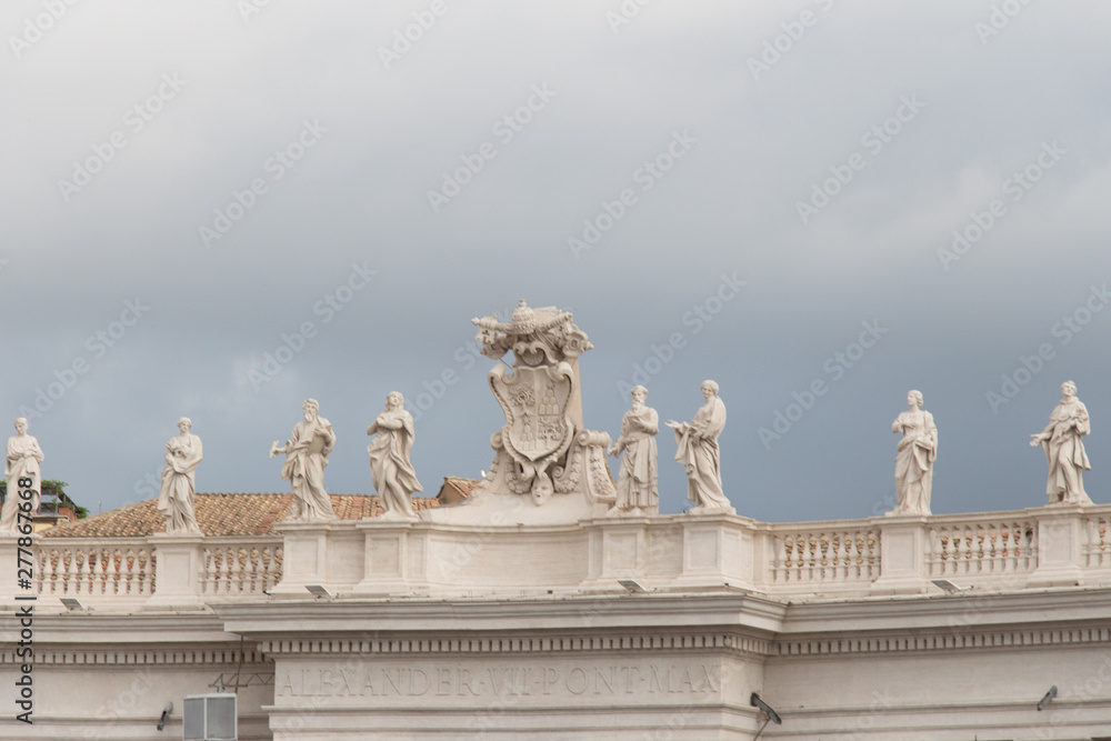 Group of statues of Peter's Square Colonnade with rainy clouds on background, Vatican city state, Italy.