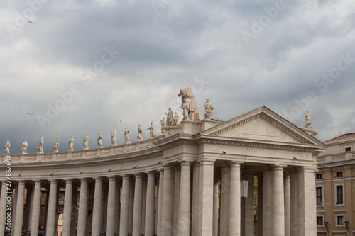 Upper facade of Peter's Square Colonnade with rainy clouds on background, Vatican city state, Italy.