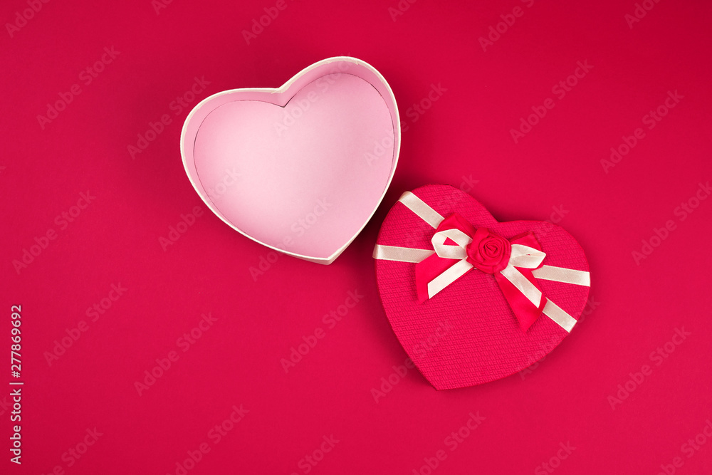 open red heart-shaped gift box with a bow on a red background
